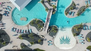 Eine Vogelperspektive zeigt ein Resort mit einem großen zentralen Pool, mehreren kleineren Pools und zahlreichen Liegestühlen rund um die Becken.