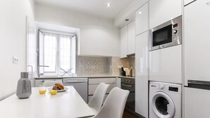 A modern kitchen with white cabinetry, a built-in microwave, an oven, and a front-loading washing machine.