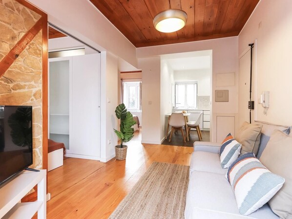 Un salon moderne avec un mur d’accent en pierre, un plafond en bois, un téléviseur, un canapé avec des coussins à rayures et un coin repas à l’arrière-plan.
