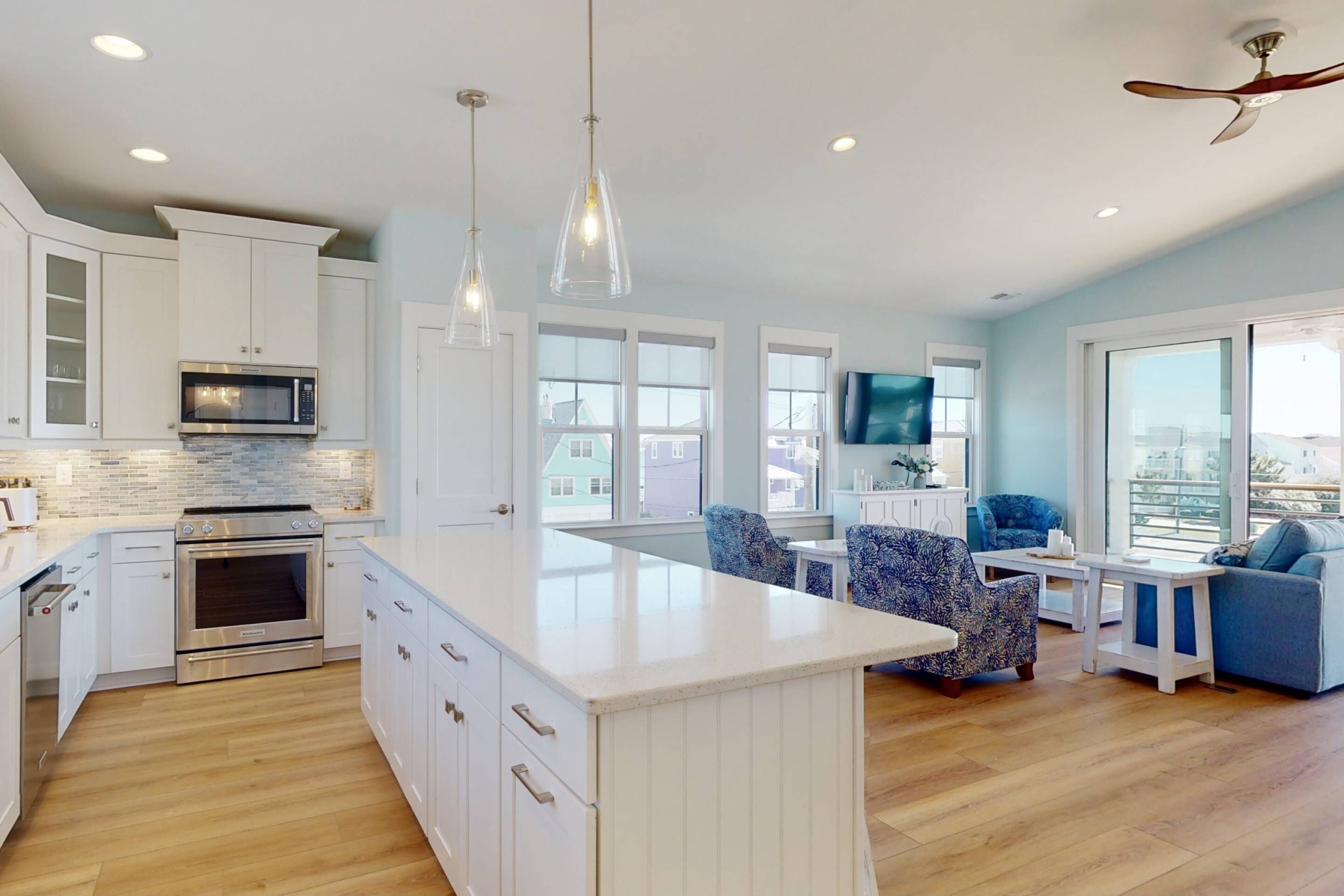 Una cocina moderna con armarios blancos, microondas integrado y horno. Hay una isla grande con encimera blanca, y la habitación tiene ventanas amplias con vistas a la ciudad.