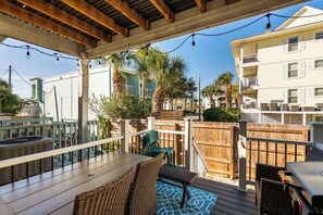 A covered outdoor deck with wicker furniture, a grill, and a wooden fence.