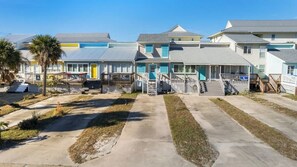 A row of beachfront condominiums with individual balconies, a central walkway, and a clear view of the ocean.