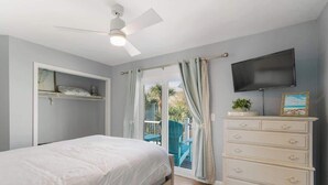 Une chambre à coucher comprenant un lit, une commode, un téléviseur et un ventilateur de plafond.