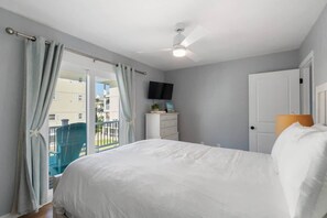 A bedroom with a bed, a TV, a dresser, and a balcony with a chair.
