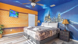 A bedroom with a bed, a ceiling fan, a TV, and a mural of a castle.