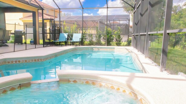 A swimming pool with a hot tub, surrounded by a covered patio area with chairs and a grill.