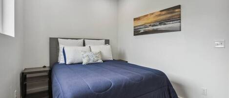 A bedroom with a bed, pillows, a nightstand, and a painting on the wall.