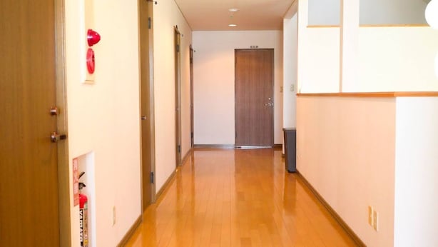 A hallway with wooden flooring, a wooden door at the end, and a fire extinguisher on the wall. - TESHIKAGA HOSTEL MISATO (Teshikaga)