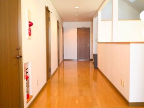 A hallway with wooden flooring, a wooden door at the end, and a fire extinguisher on the wall. - TESHIKAGA HOSTEL MISATO (Teshikaga)