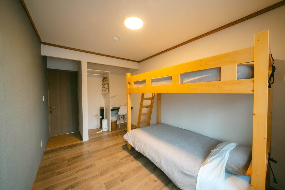 A bunk bed room with a wooden ladder, a desk, and a chair in the background.