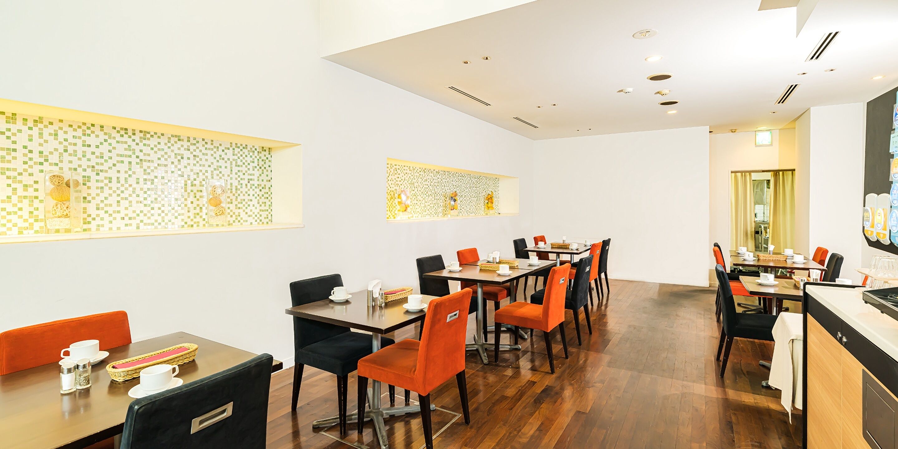 A modern dining area with multiple tables and chairs, a kitchen counter, and decorative wall panels.