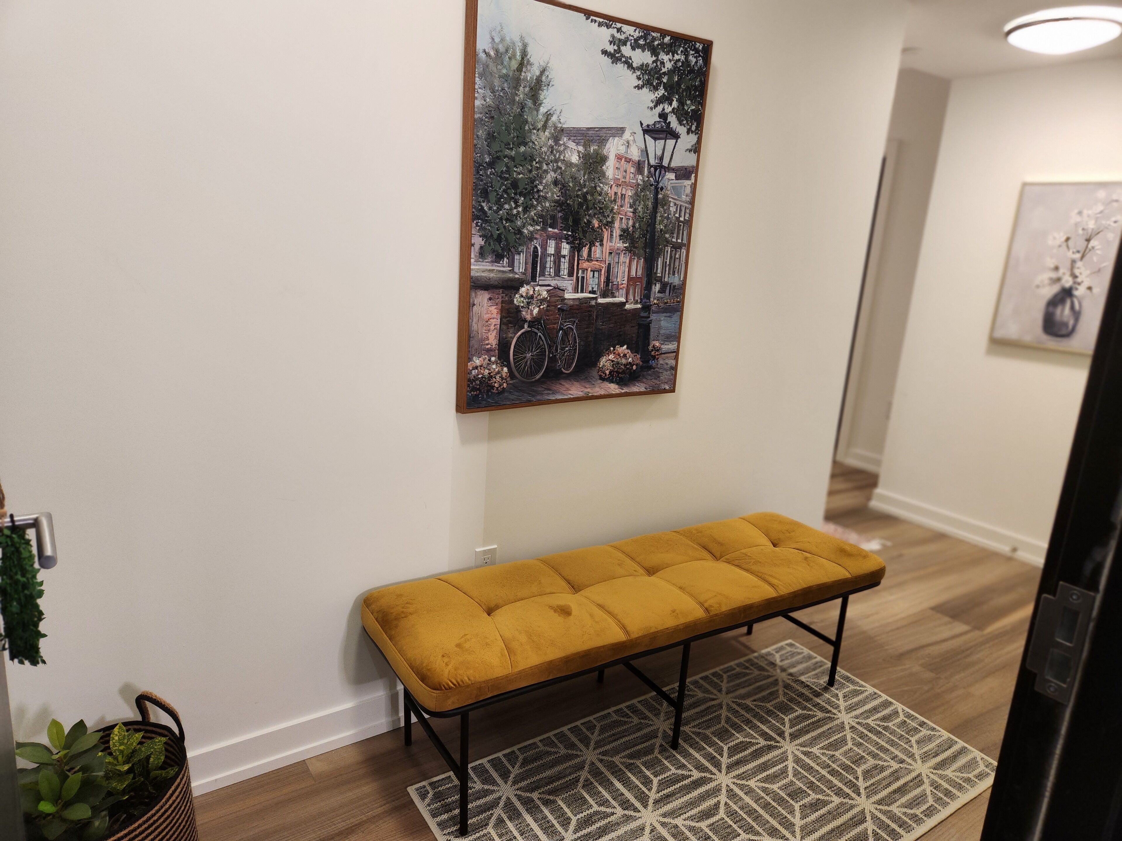 A hallway with a bench, a painting, and a patterned rug.