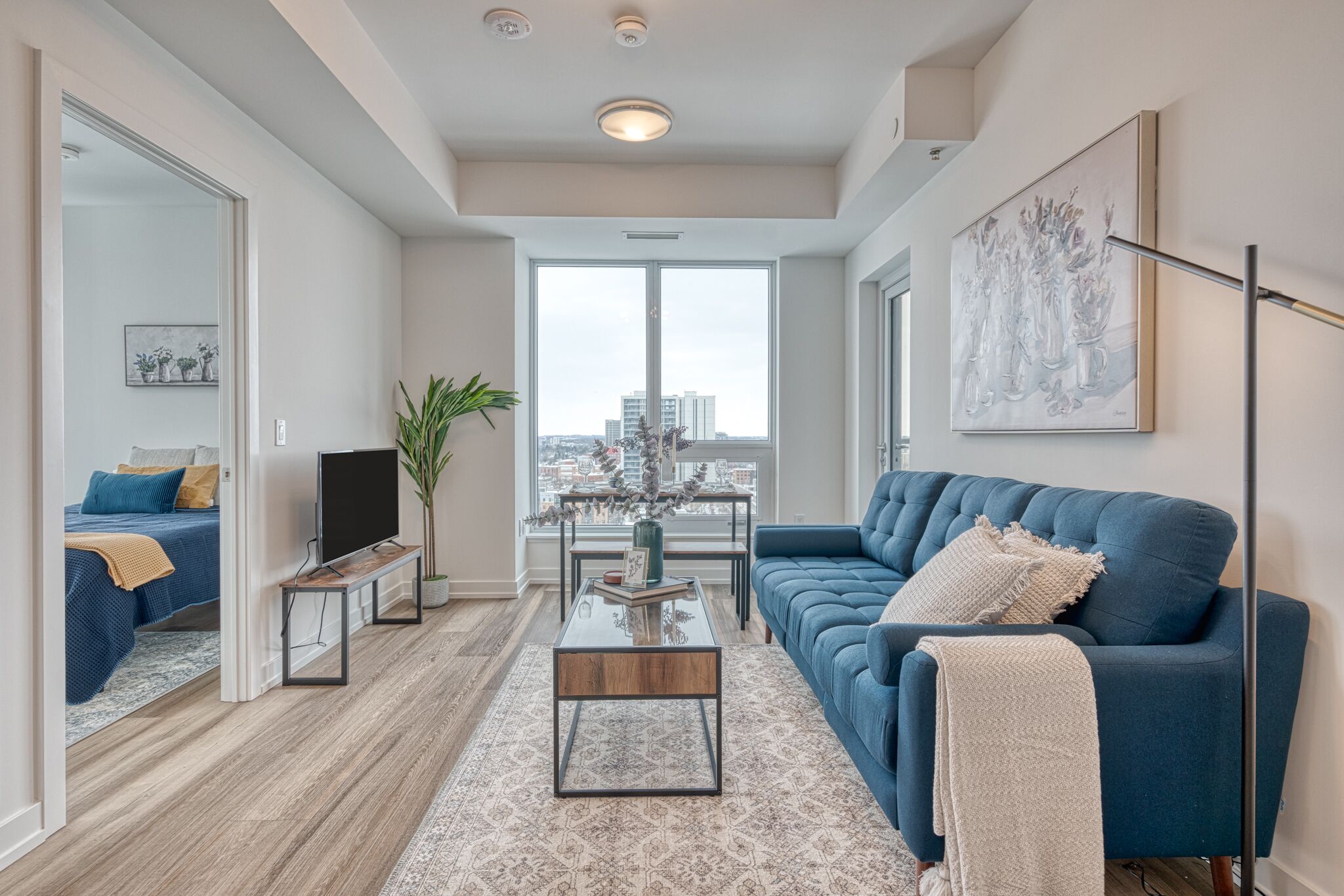 Uma sala de estar moderna com um sofá azul, uma mesa de centro e uma janela grande com vista para a cidade.