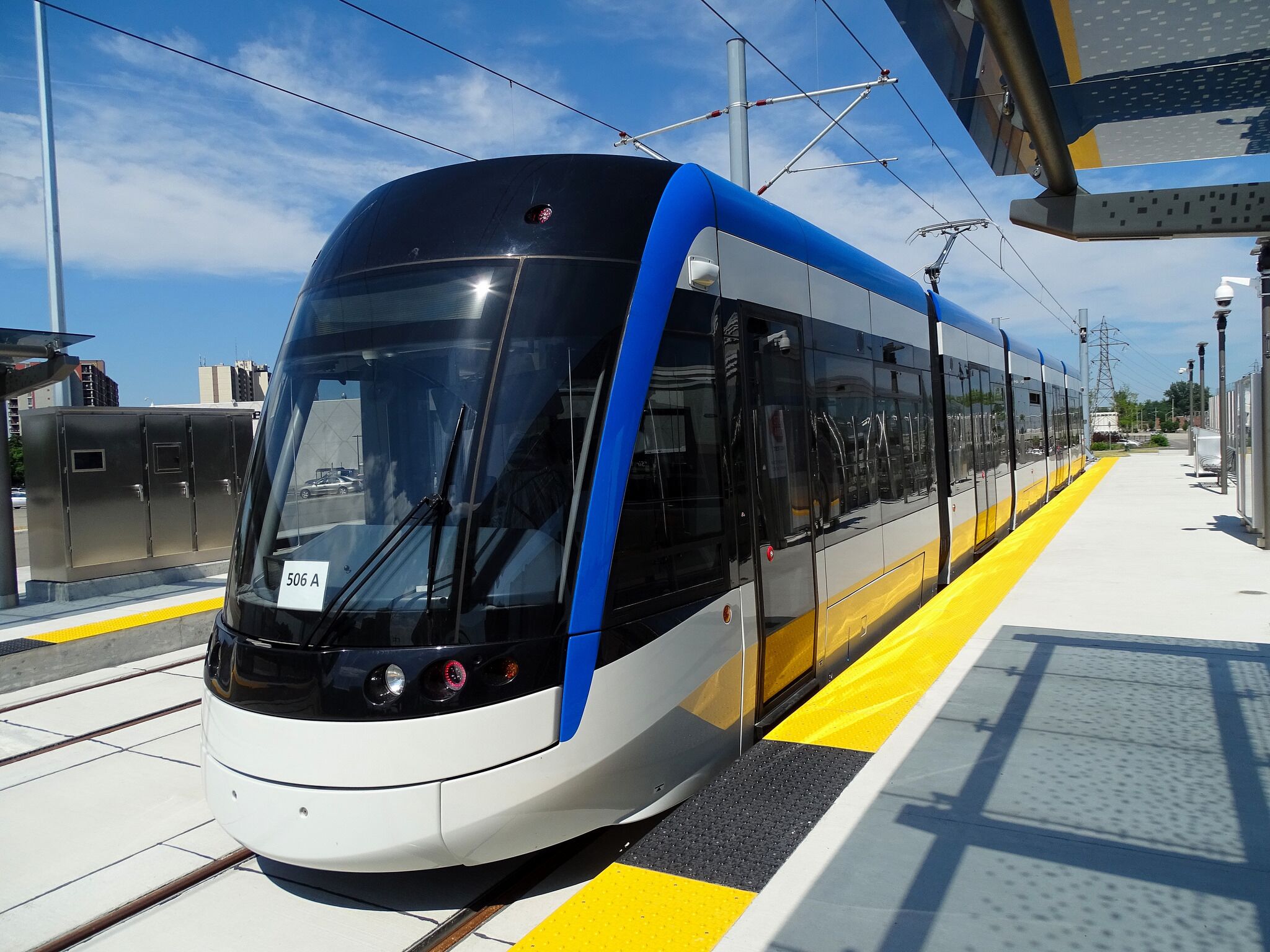 Eine moderne Straßenbahn an einer Haltestelle unter blauem Himmel.