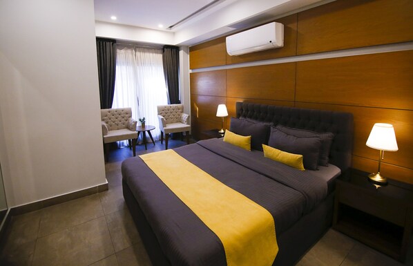 A hotel room with a large bed, two bedside lamps, a small table with a chair, and a window with curtains. - Space Suites (Rawalpindi)