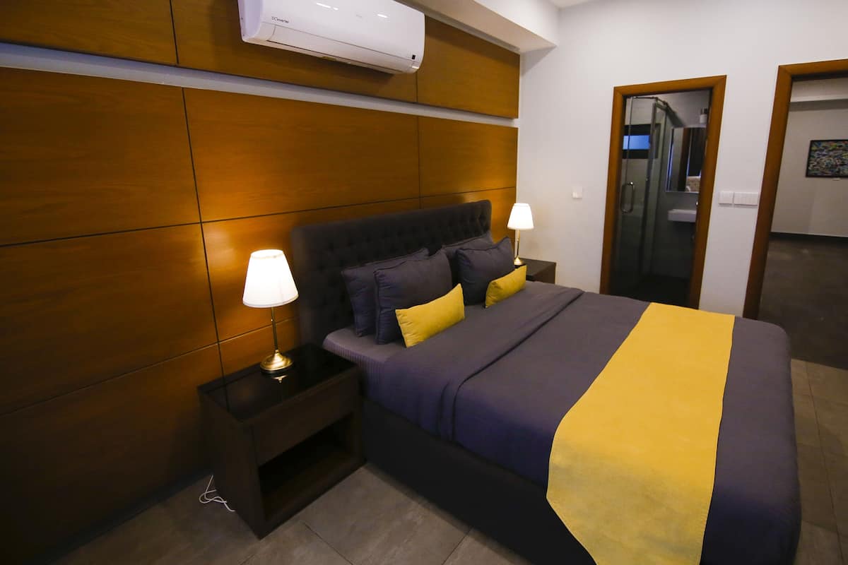 A hotel room with a bed, nightstands, a lamp, and an air conditioning unit.