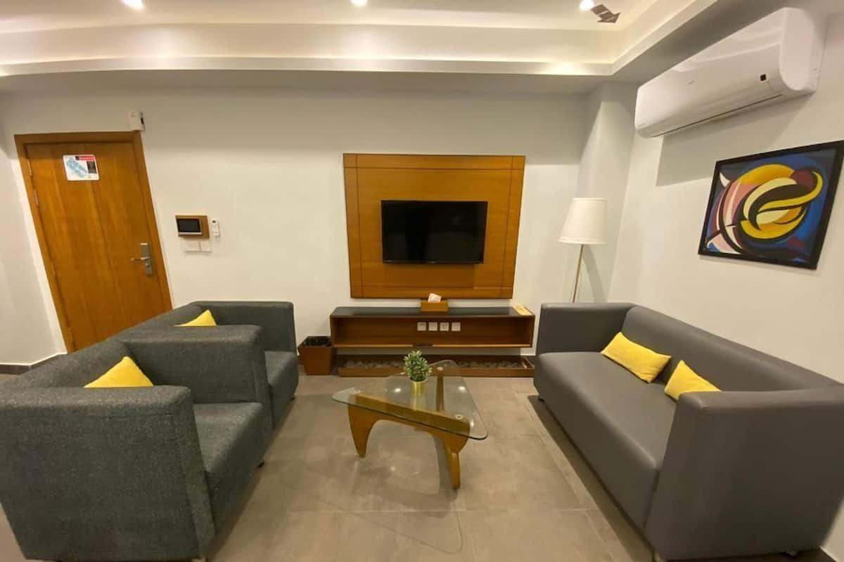 A modern living room with grey sofas, a wooden entertainment unit, a flat-screen TV, and a painting on the wall.