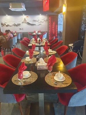 A restaurant with a long table set for dining, red chairs, and a decorative wall with a mountain and pagoda painting. - Space Suites (Rawalpindi)