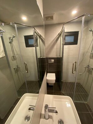 A modern bathroom with a glass-enclosed shower, a white toilet, and a large sink with a mirror. - Space Suites (Rawalpindi)