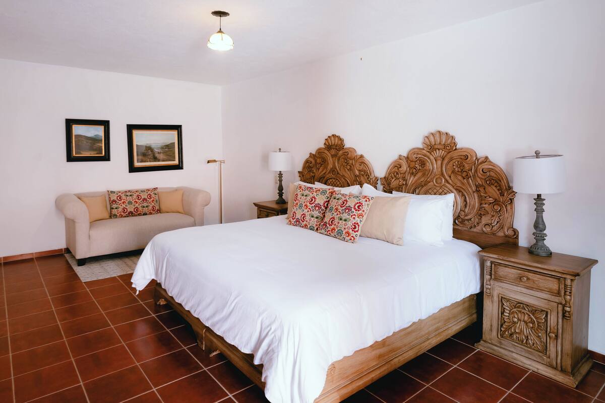A bedroom with a bed, a nightstand, a bedside table, a lamp, a sofa, and two framed pictures on the wall.