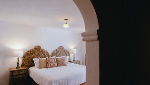 A bedroom with a large bed, ornate headboard, two bedside tables with lamps, and a hanging light fixture.