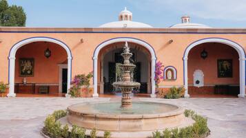 Un patio con una fuente central, arcos y un edificio con cúpula y columnas.
