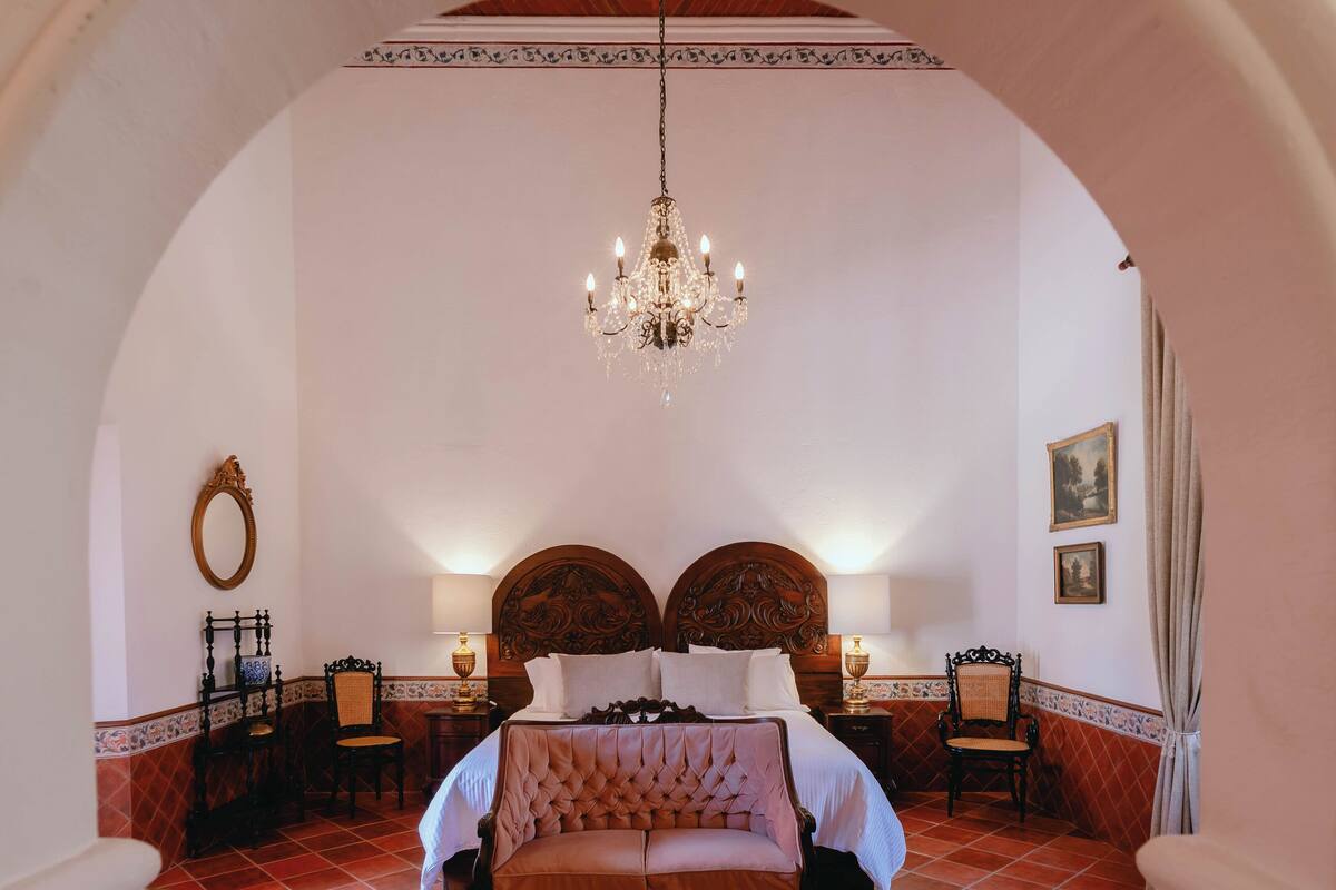 A bedroom with a large bed, ornate headboard, chandelier, and classic decor.