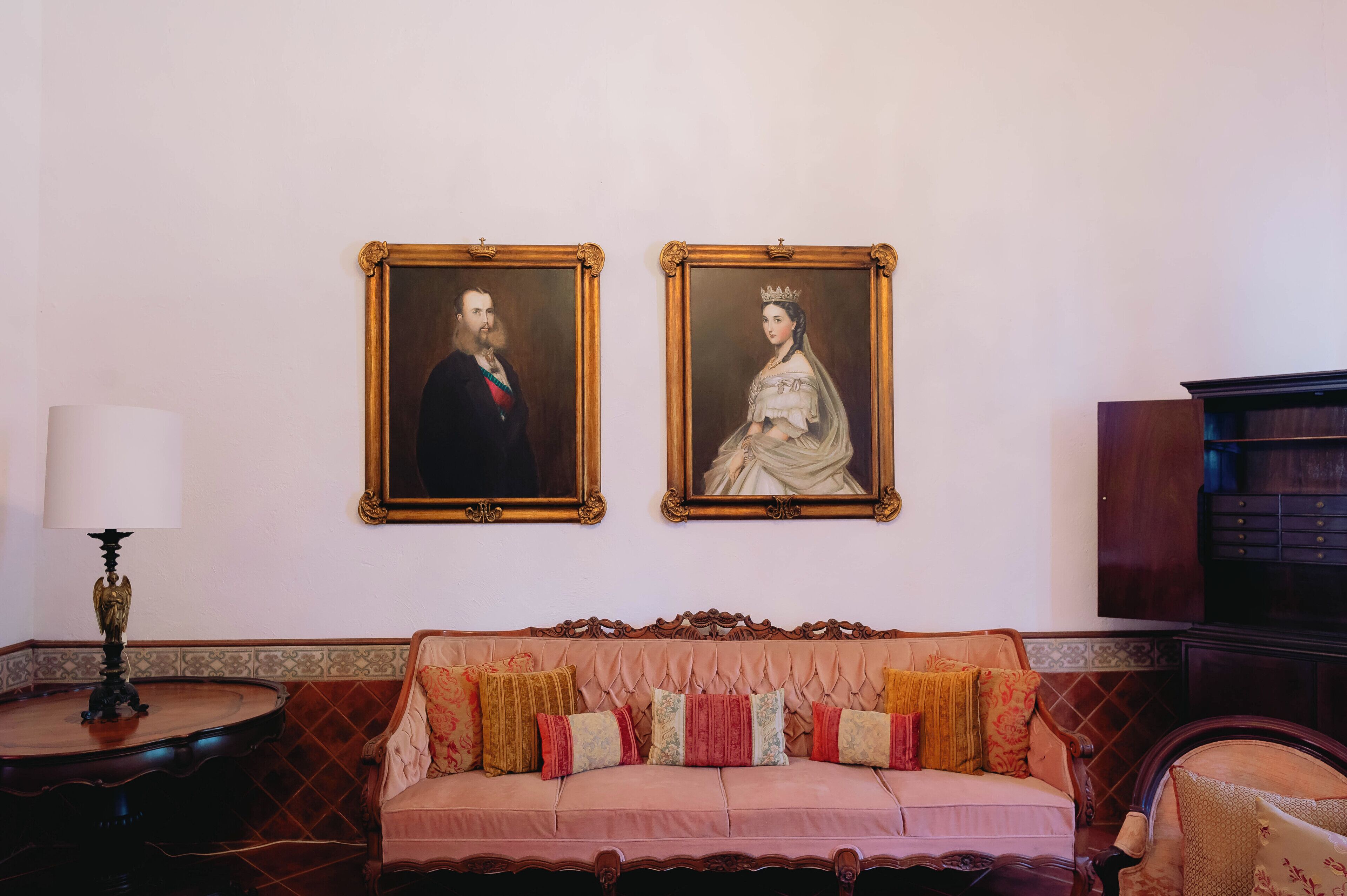 A room with a sofa, a round table, and two framed portraits on the wall.