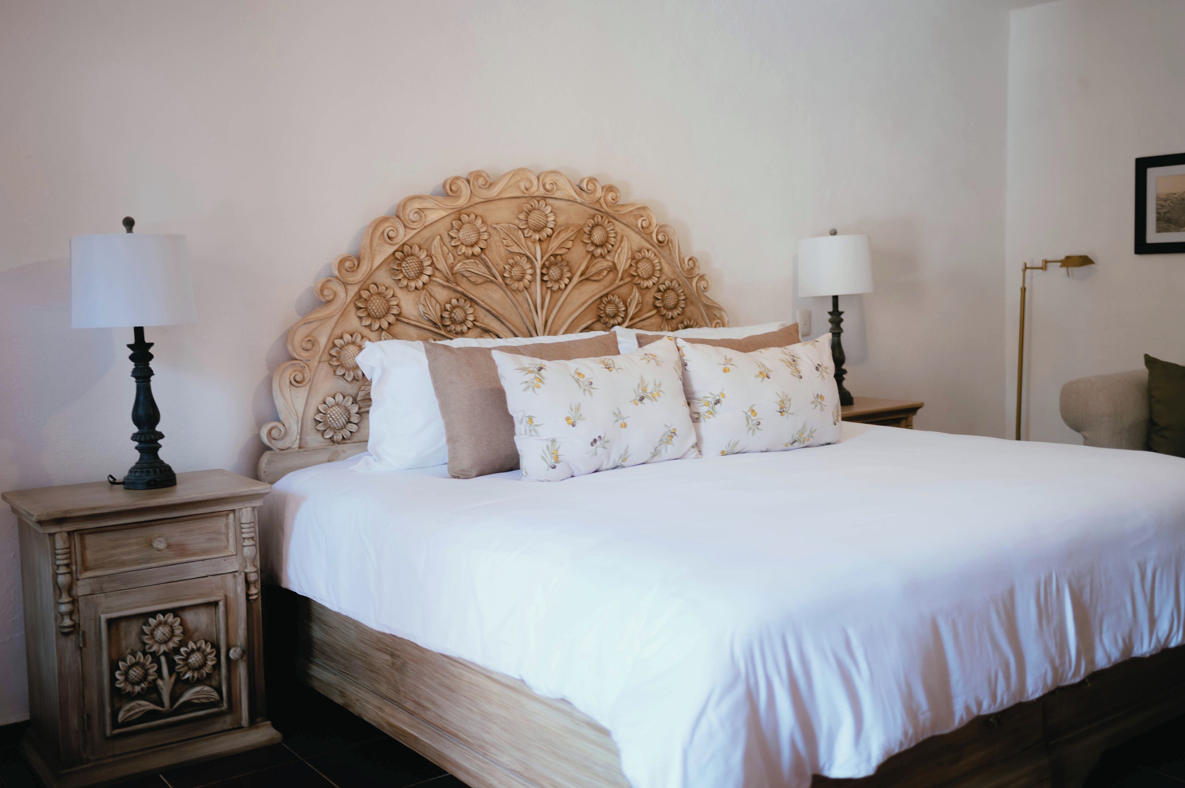 A neatly made bed with a floral headboard, two bedside tables with lamps, and a small cabinet with floral carvings.