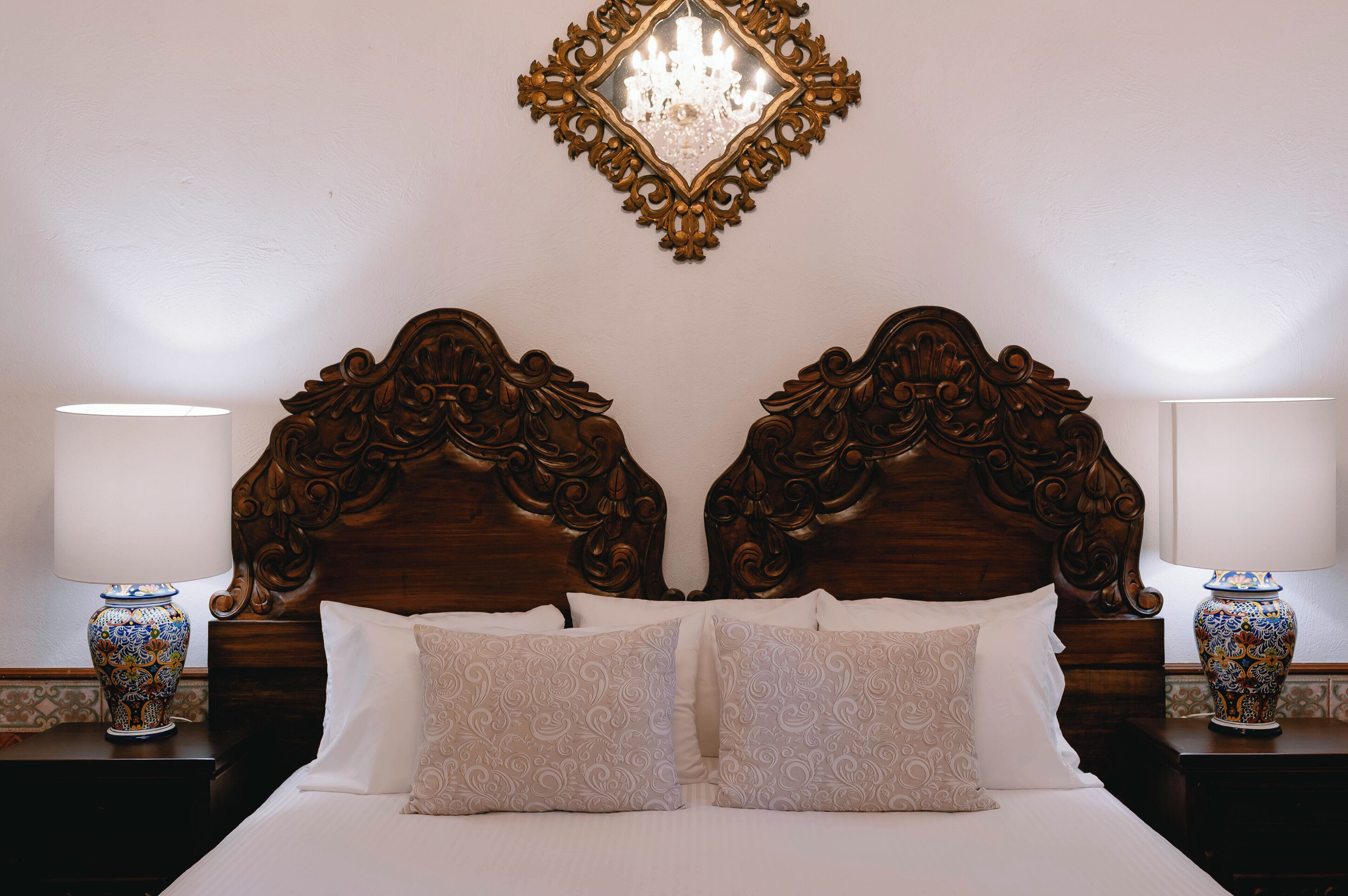 A bed with a wooden headboard, two bedside tables with lamps, and a decorative mirror above the bed.