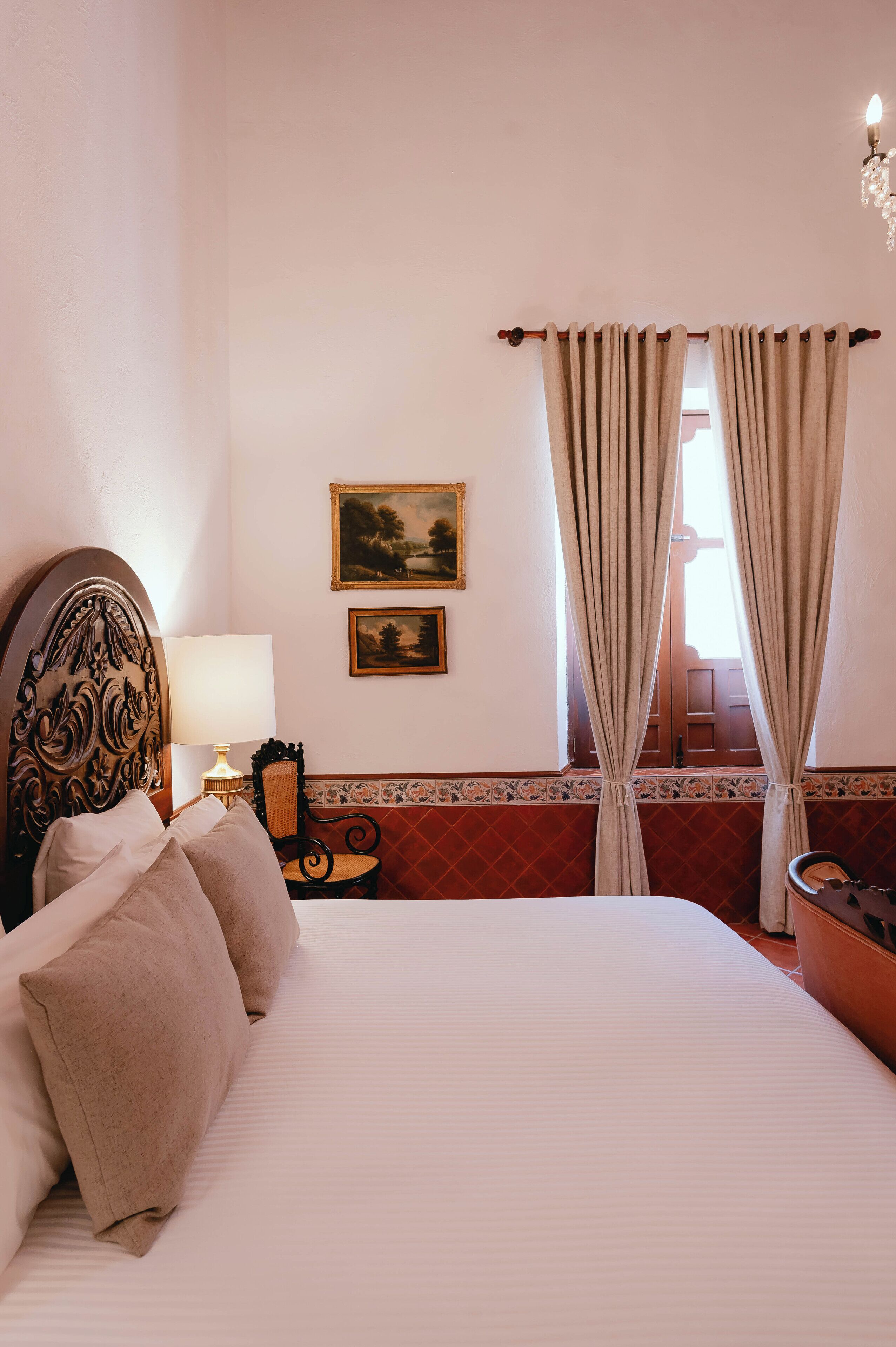 A neatly made bed with a headboard, a bedside table with a lamp, and two framed pictures on the wall.