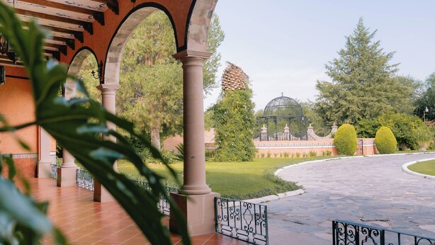 A covered outdoor area with arches, a stone pathway, and a garden with trees and a dome structure.