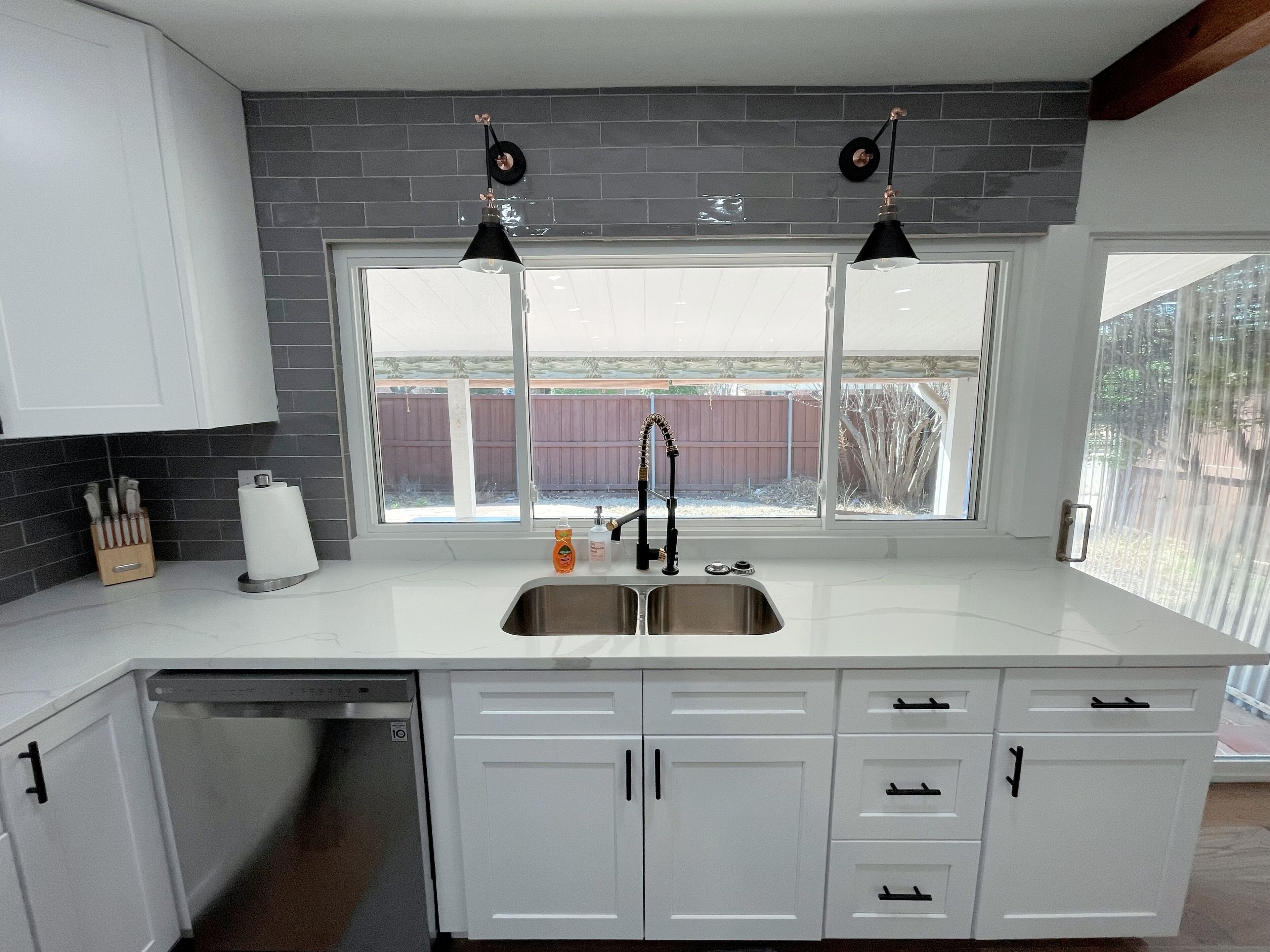 A modern kitchen with white cabinets, a stainless steel sink, and two pendant lights.