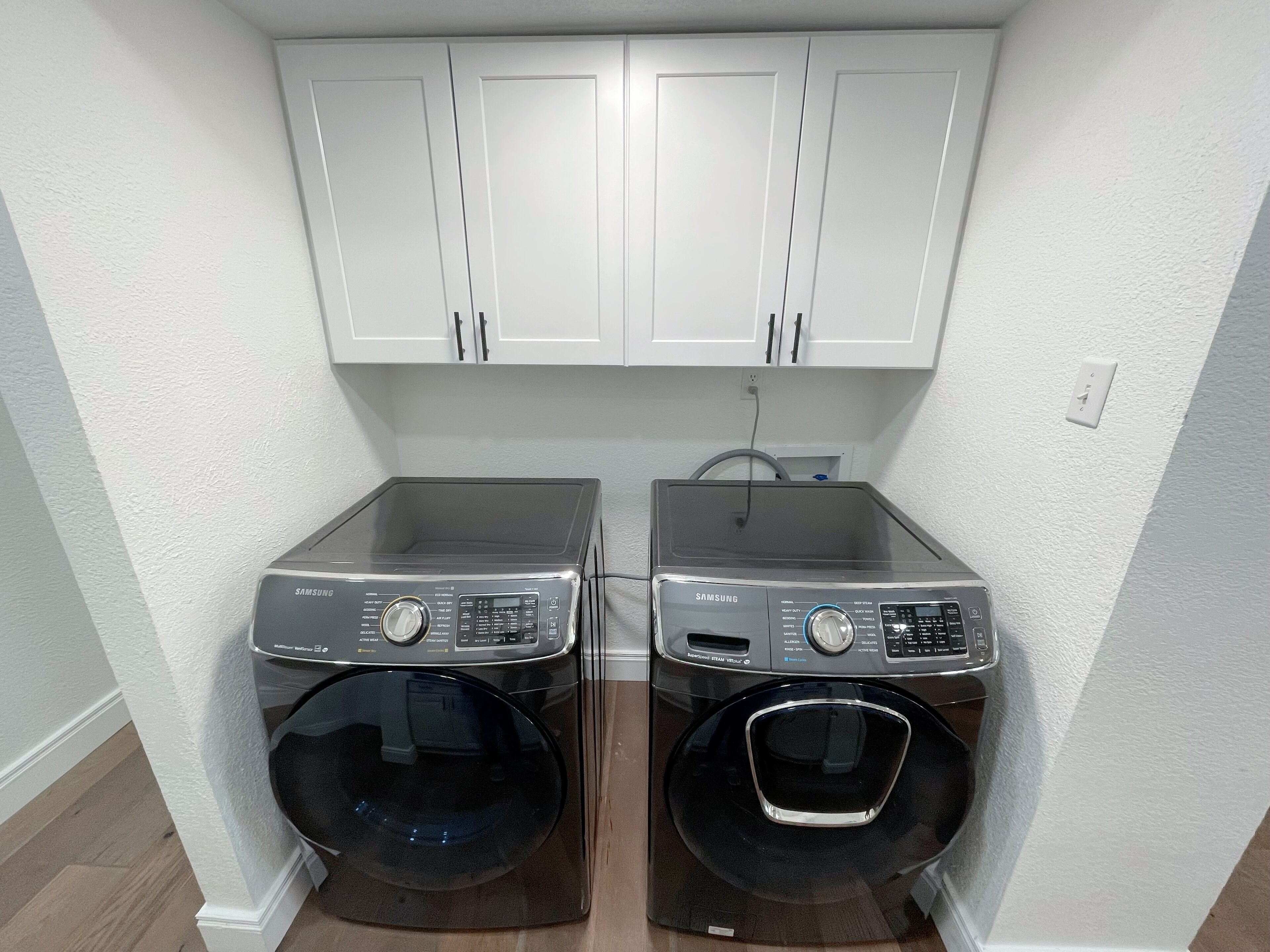 Une buanderie équipée de deux lave-linge Samsung à chargement frontal et de meubles blancs fixés au mur au-dessus.