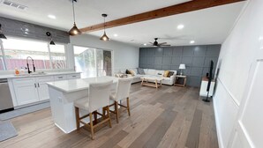 Une cuisine moderne avec un îlot central, un coin repas avec un canapé et des chaises, et un salon équipé d’une télévision et d’une lampe.