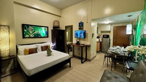 A modern bedroom with a bed, bedside table, and a TV. There is a dining area with a table and chairs, and a kitchen in the background. - Beautiful Studio Near Resorts World NAIA T3 (Pasay)