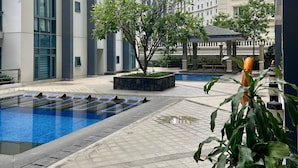 A modern hotel courtyard with a swimming pool, potted plants, and high-rise buildings in the background. - Beautiful Studio Near Resorts World NAIA T3 (Pasay)