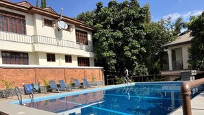 Una piscina con sillones de descanso, un muro de ladrillo y un edificio con balcón.
