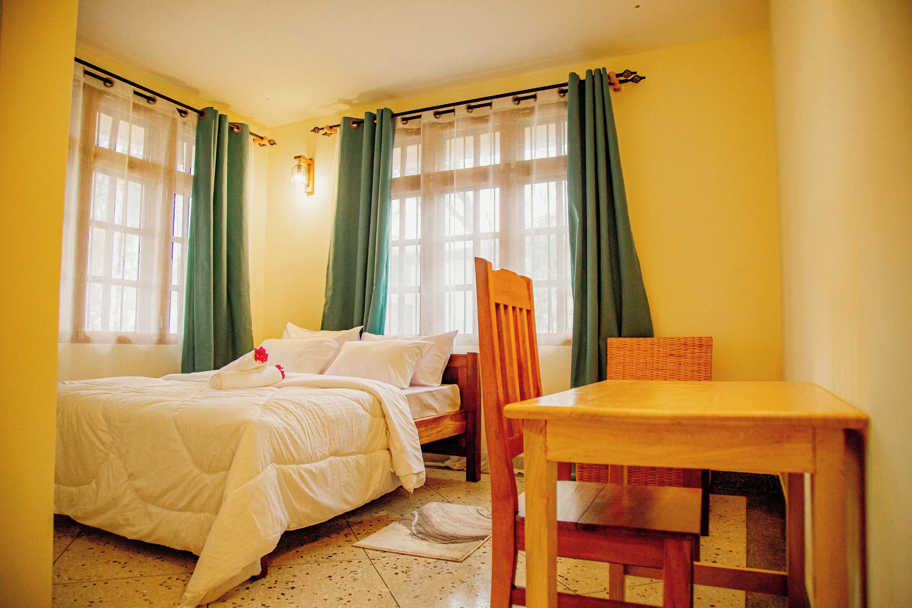 A bedroom with a bed, a wooden chair, a small table, and a window with curtains.