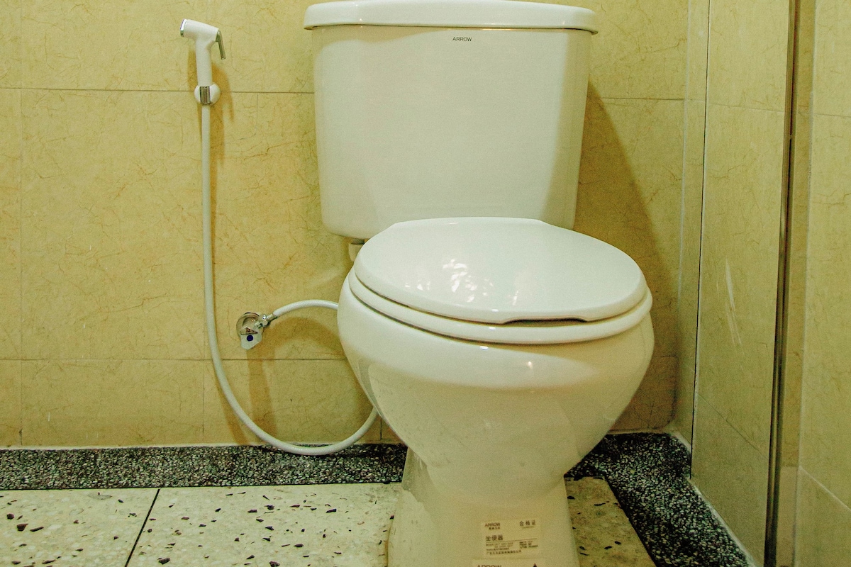 A toilet with a bidet attachment in a bathroom with tiled walls and floor.