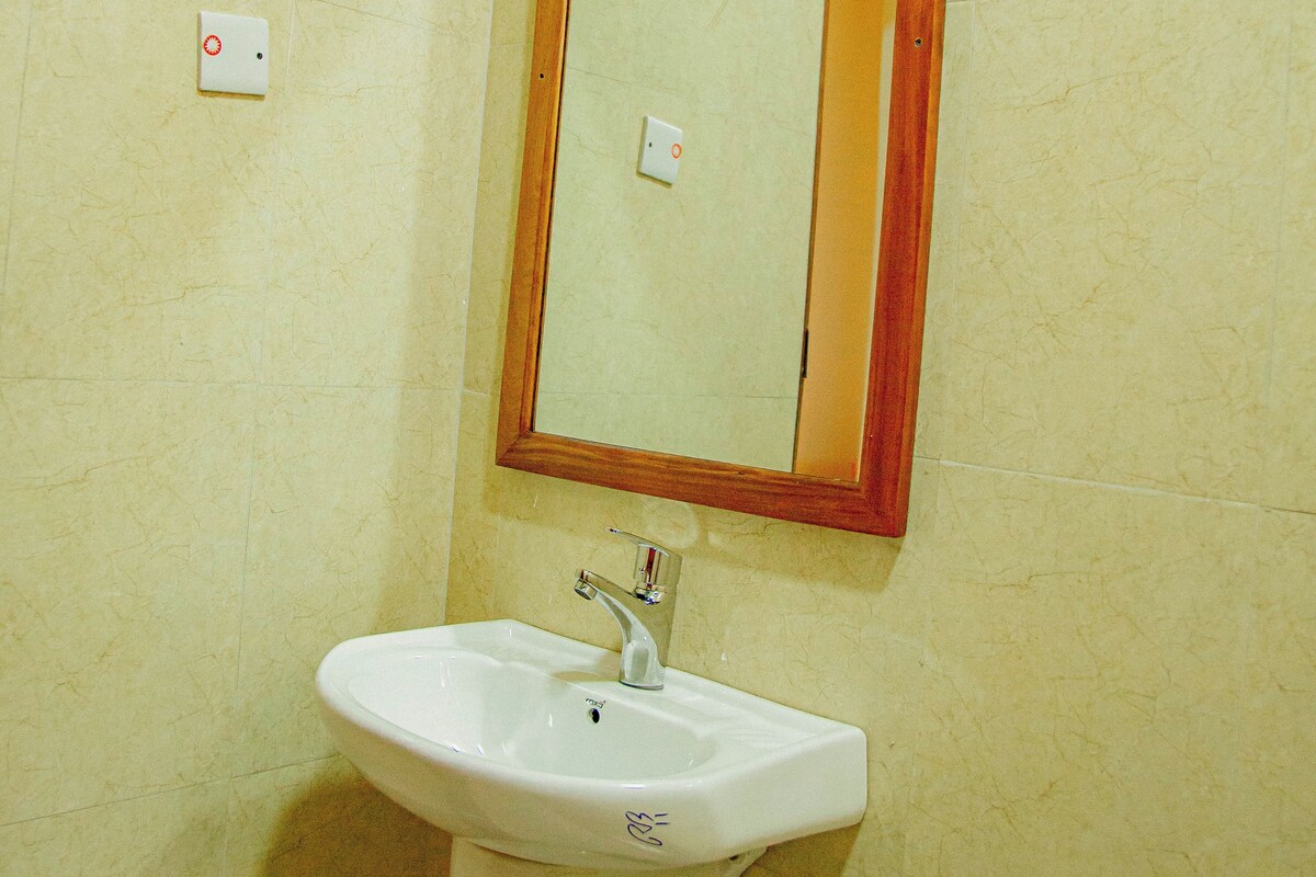 A bathroom with a white sink, a mirror with a wooden frame, and a light switch on the wall.