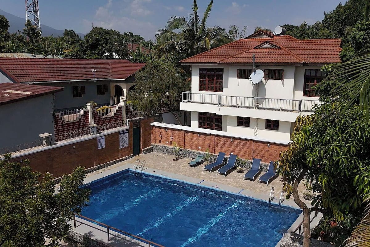 Un área de piscina con una piscina azul cristalina, sillones de descanso y un edificio de dos pisos con techo rojo y paredes blancas.