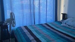 Ein Schlafzimmer mit einem Bett, einem Schreibtisch und einem Standventilator.