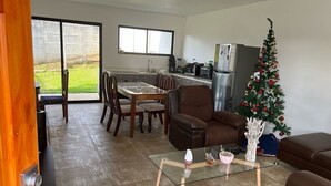 Ein modernes Wohnzimmer mit einem Glastisch, einer braunen Ledersofa und einem Essbereich mit Tisch und Stühlen. In der Ecke steht ein Weihnachtsbaum.