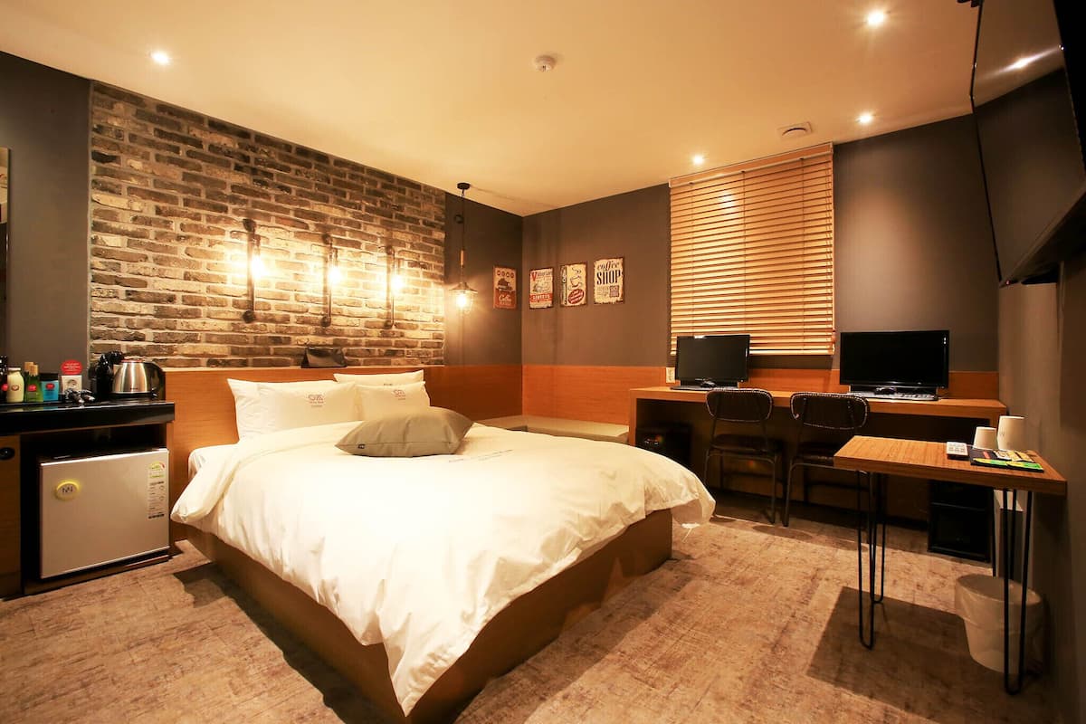 Ein Hotelzimmer mit Backsteinwand, einem Bett mit weißer Bettwäsche, einem Schreibtisch mit Computer und einer kleinen Küchenzeile.