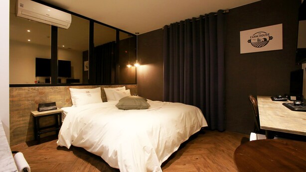 Une chambre d’hôtel avec un grand lit, une petite table de chevet, un bureau avec une chaise, un miroir et un climatiseur fixé au mur.