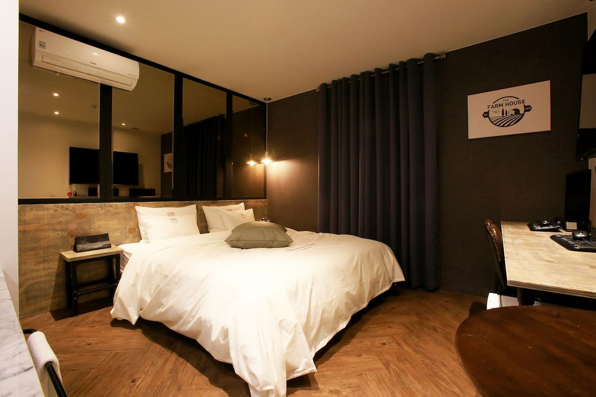 Ein Hotelzimmer mit einem großen Bett, einem kleinen Nachttisch, einem Schreibtisch mit Stuhl, einem Spiegel und einer Wand-Klimaanlage.