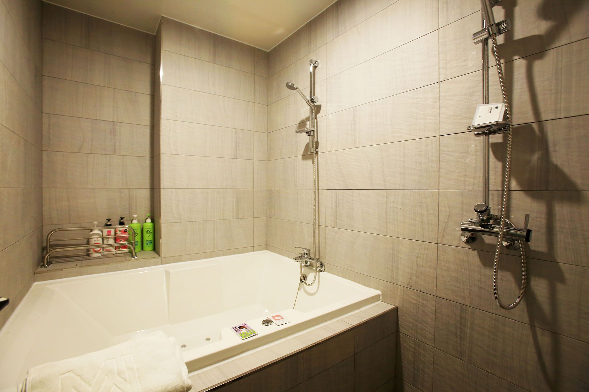 Un baño moderno con bañera, ducha y un perchero con artículos de aseo.