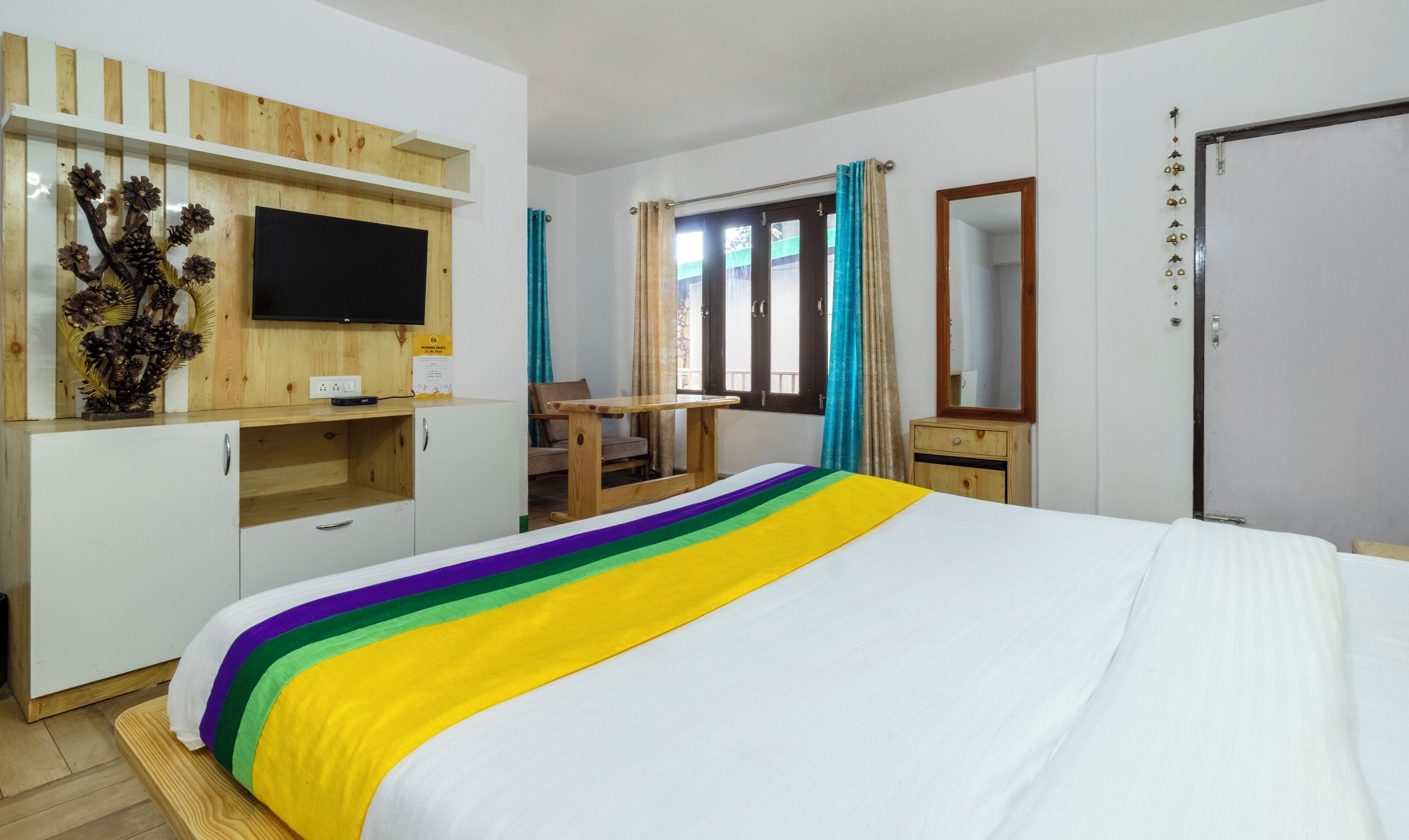 A hotel room with a bed, a desk, a TV, a wardrobe, and a window with curtains.