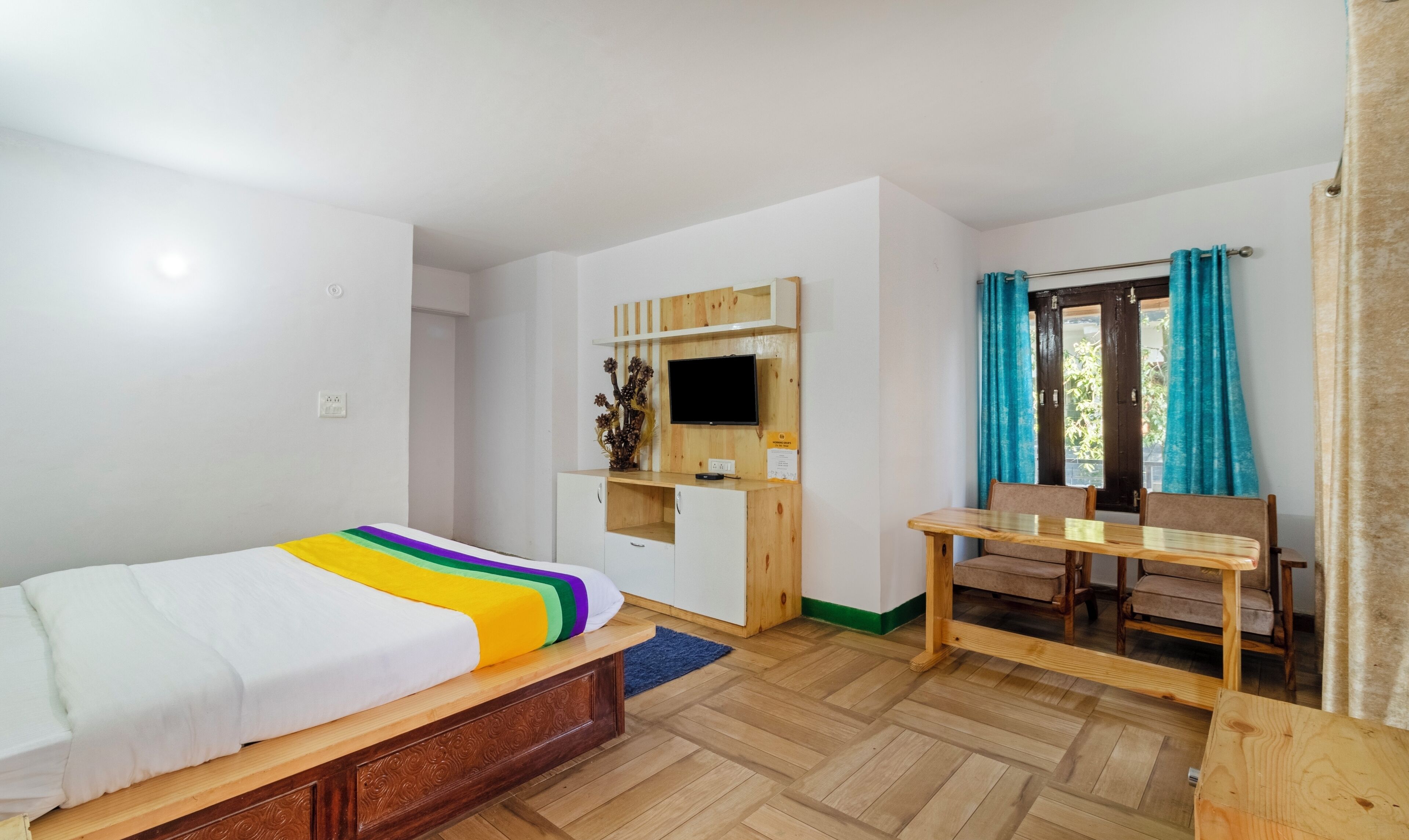 Une chambre avec un lit, un bureau, une télévision et une fenêtre avec des rideaux.